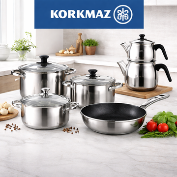 Korkmaz cookware collection featuring stainless steel pots, pans, pressure cooker, and tea set on modern kitchen countertop with elegant setup